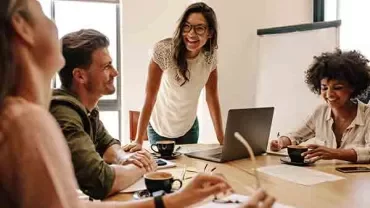 Team in office having a discussion with laptops and coffee.