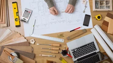 Person drawing architectural plans at a desk with various tools.
