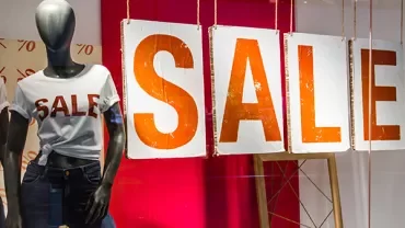 Mannequin in jeans and sale t-shirt beside large sale signs in store window.