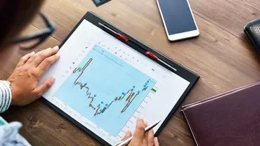 Person analyzing a financial chart on a tablet at a desk.
