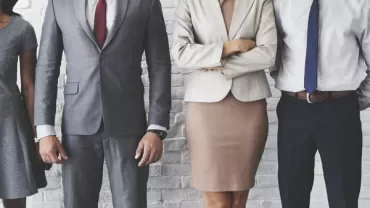 Four people standing in business attire against a white brick wall.