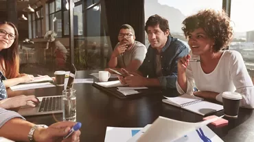 Group of people having a meeting around a table with laptops and notebooks.