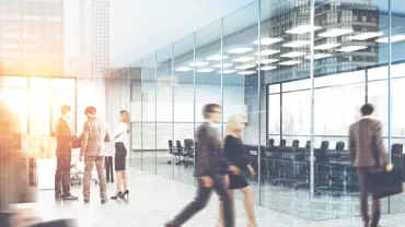 People walking in a modern glass office building with a bright interior.