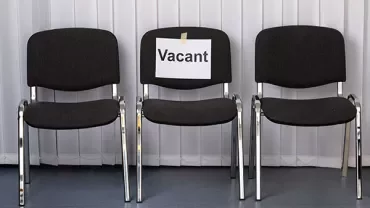 Three black chairs in a row, middle chair with a 'Vacant' sign taped to the back.