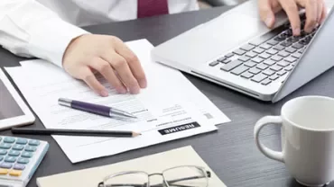 Person typing on a laptop with documents and coffee on a desk.