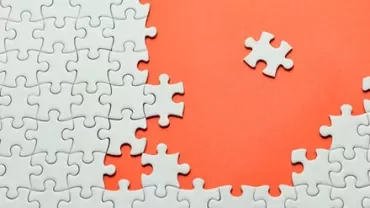 A nearly completed white puzzle on an orange background with one missing piece.