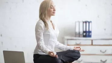 Person meditating on a desk in a serene office setting with a laptop and notebooks nearby.