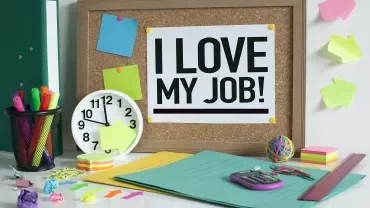Desk scene with a bulletin board saying 'I love my job!' above office supplies.