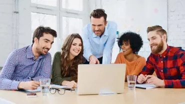 A group of people gathered around a laptop in a bright office.