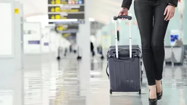 Person walking in an airport with a rolling suitcase.