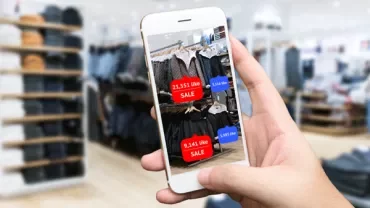 Person holding a phone showing clothing items on sale with likes in a store.