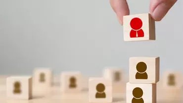 Hand stacking wooden blocks with human icons, one highlighted in red.