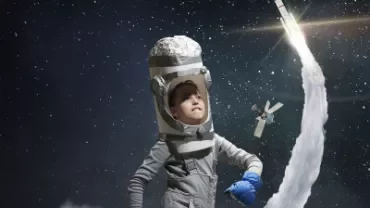 Child in homemade astronaut costume gazing at space rocket.