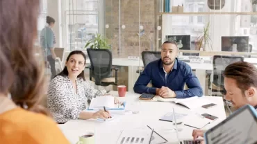 Team meeting in a bright office with people discussing at a table.