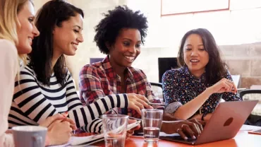 Group of people smiling and discussing around a laptop.