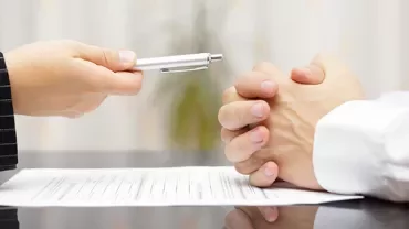Person handing a pen over a document on a table.