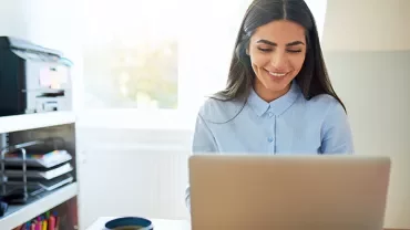 Person smiling and working on a laptop at a desk.