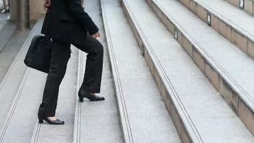 Person in business attire ascending outdoor steps with a briefcase.