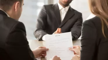 Two people interview a candidate holding a resume.