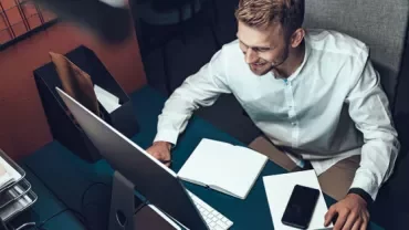 Person working at a desk with a computer, notebook, and phone.