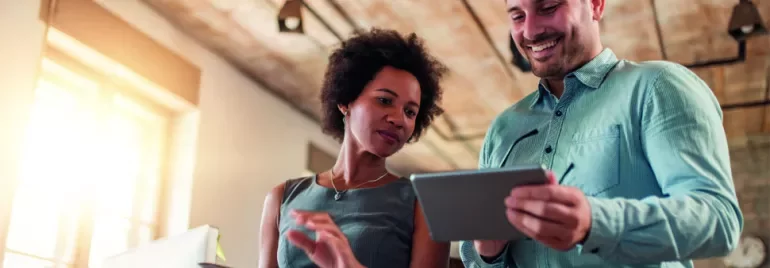 Two people looking at a tablet in a bright office setting.