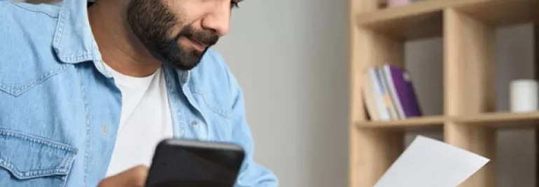 Person reading a paper while holding a phone, with a mug on the table.