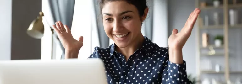 Person smiling and looking at a laptop, raising hands in excitement.