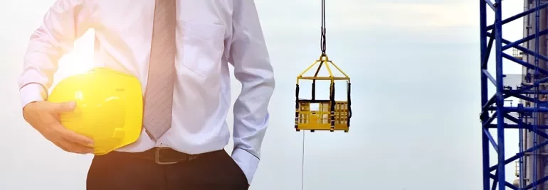 Person holding a yellow hard hat at a construction site with a crane in the background.