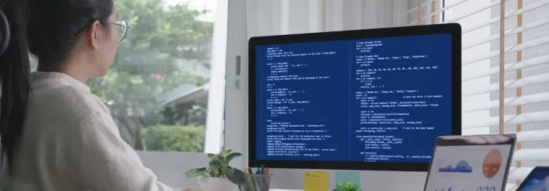 Person working on computer with code on screen, next to a window with plants.