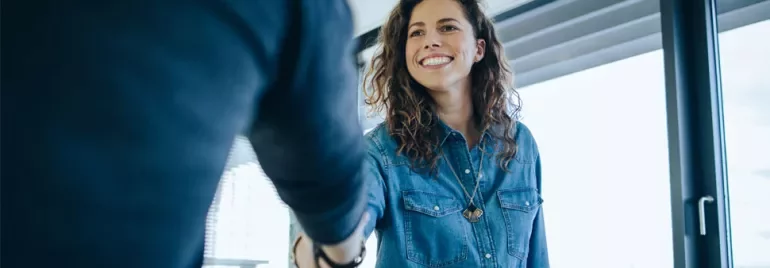 Person in denim shirt smiling and shaking hands.