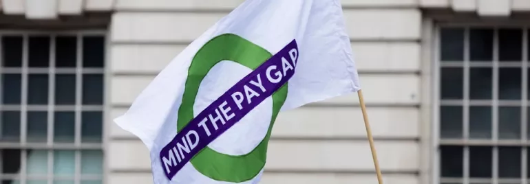 White flag with a green circle and 'Mind the Pay Gap' text in front of a building.