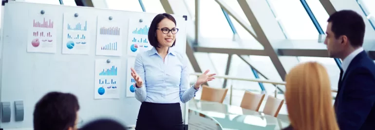 Person giving a presentation with charts on a whiteboard in a modern conference room.