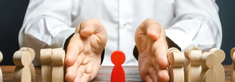 Hands separating a red figure from wooden figures on a table.