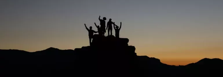 Silhouette of people celebrating on a hill during sunset.