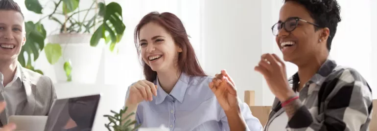 Three people sitting at a table, smiling and laughing during a meeting.