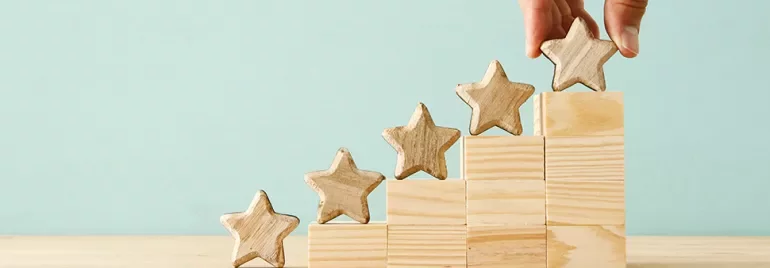 Hand placing wooden star on blocks arranged in steps.