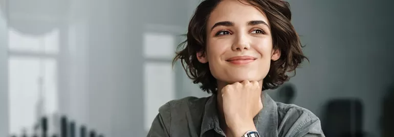 Person with short hair smiling, wearing a wristwatch, thoughtful pose.