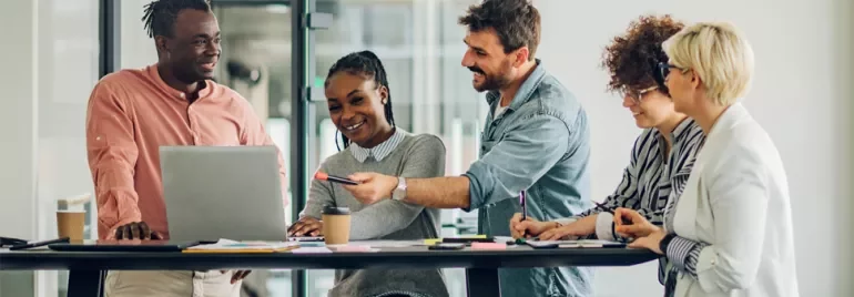 Group of people collaborating in an office setting with laptops and notes.