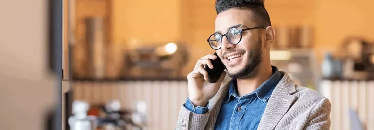 Person smiling and talking on a smartphone indoors.