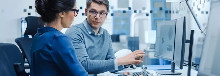 Two colleagues discussing work at a computer in an office.