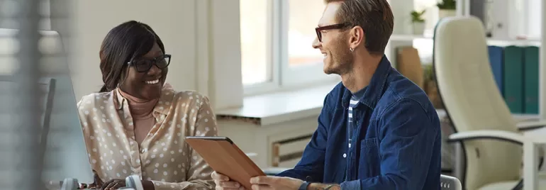 Two colleagues smiling and discussing work in a bright office.