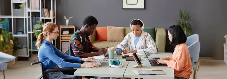 Group of four people working together at a table with laptops and notebooks.