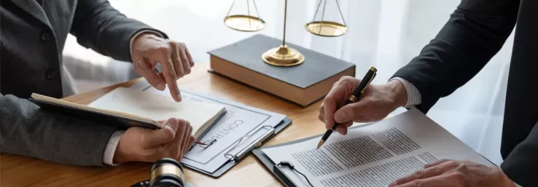 Two people reviewing a contract at a desk with law books and a gavel.