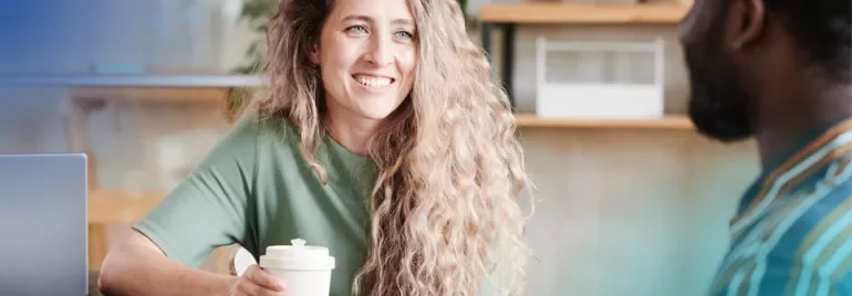 A woman and a man sit at a table, focused on a laptop in front of them, engaged in discussion or collaboration.