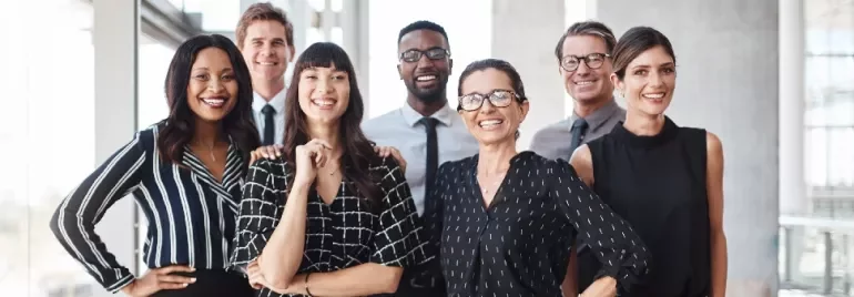 Diverse group of professionally dressed adults smiling in a office setting.