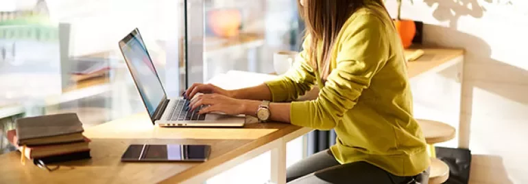 Person working on a laptop at a bright, cozy cafe.