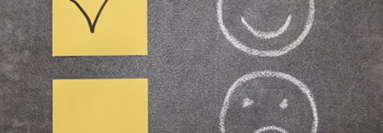 Yellow sticky notes with a check mark and boxes, chalk smiley and sad face on a blackboard.