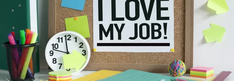 Desk scene with a bulletin board saying 'I love my job!' above office supplies.