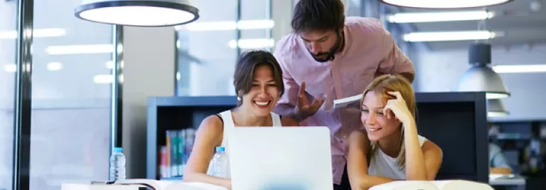 Group of friends studying together at a library table with a laptop.