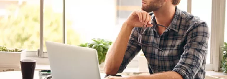 Person sitting at a desk with a laptop, looking out the window.